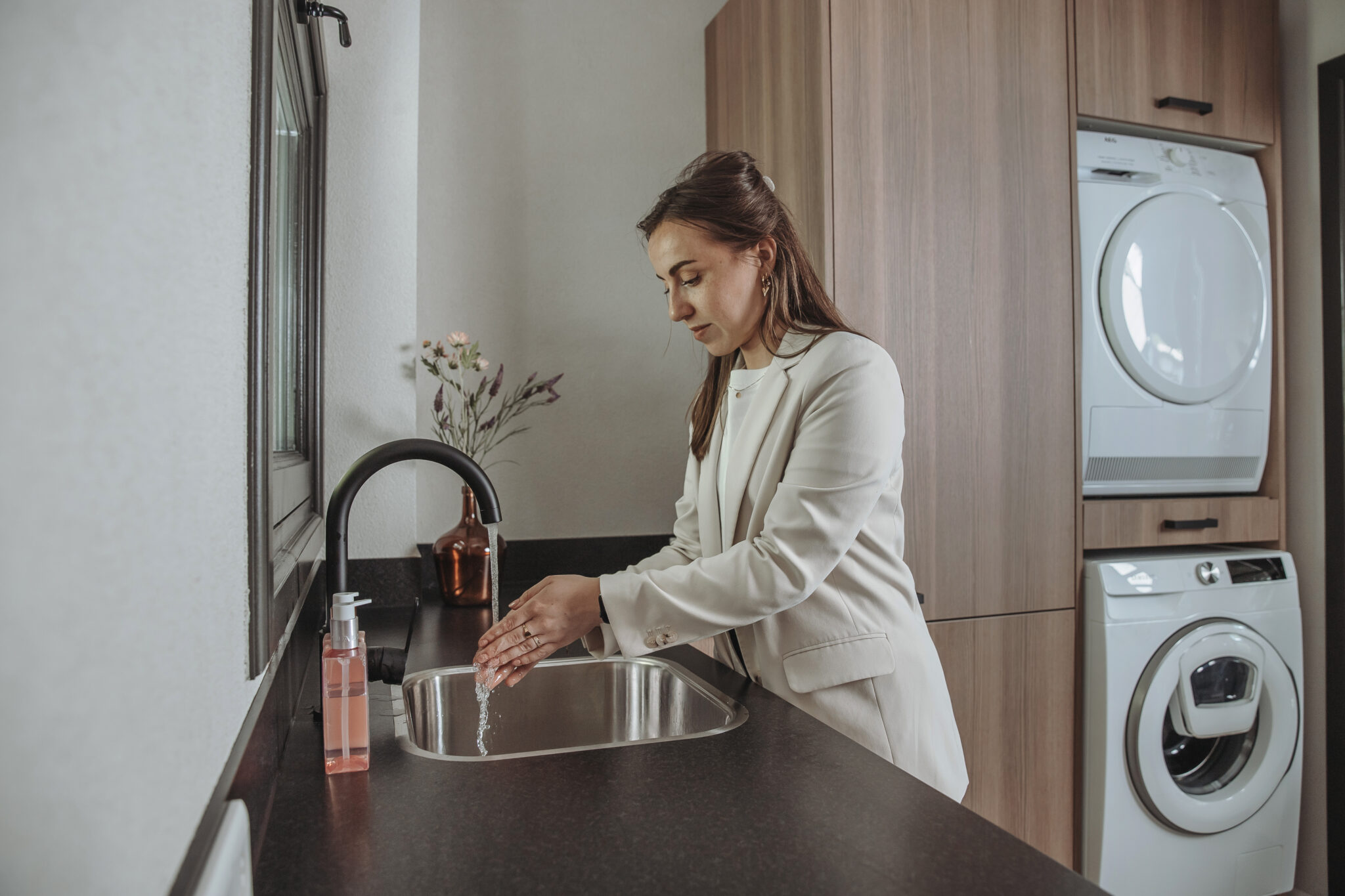 Vrouw bij een wasbak met een wasmachinekast op de achtergrond.